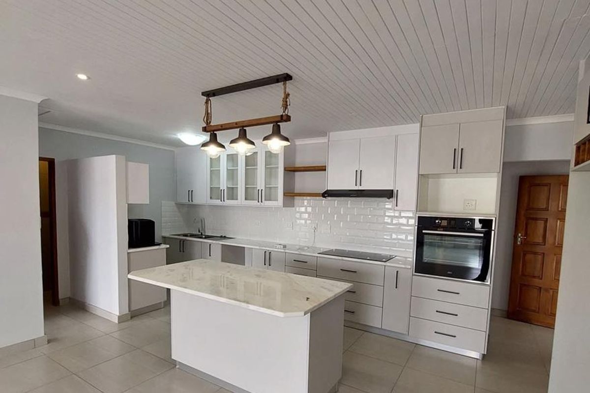 Modern open-plan kitchen featuring white cabinetry, stone countertops, a central island, built-in oven, and subway tile backsplash.