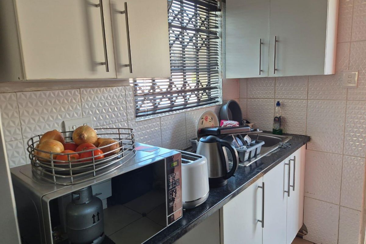 Compact kitchen featuring white cabinetry, dark countertops, tiled backsplash, and a window with security bars.