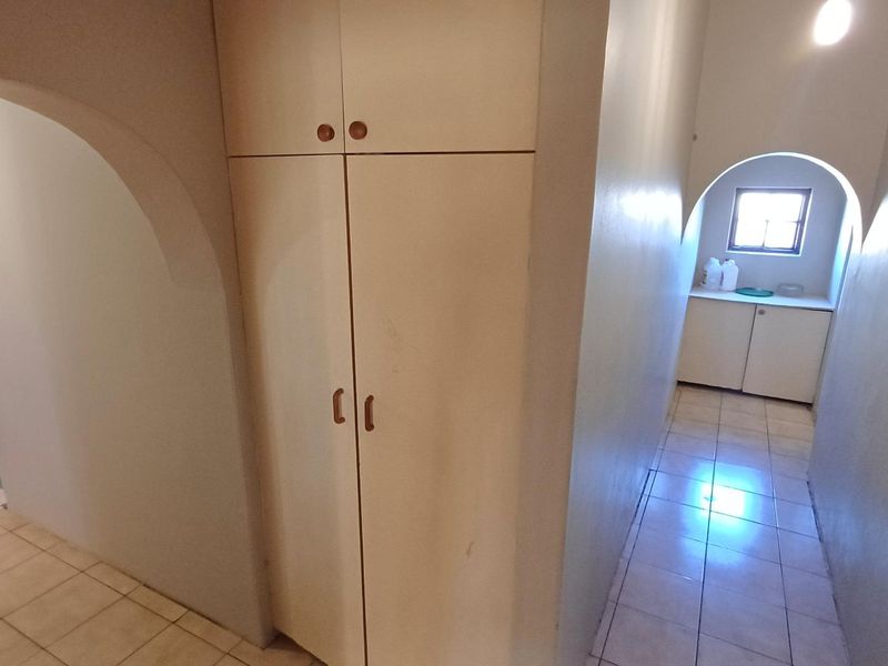 A functional hallway featuring built-in storage cupboards, tiled flooring, and distinctive arched architectural details leading to adjacent rooms.