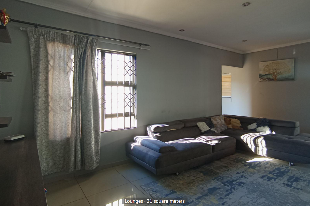 A spacious living room featuring tiled flooring, recessed ceiling lighting, and security bars on the windows.