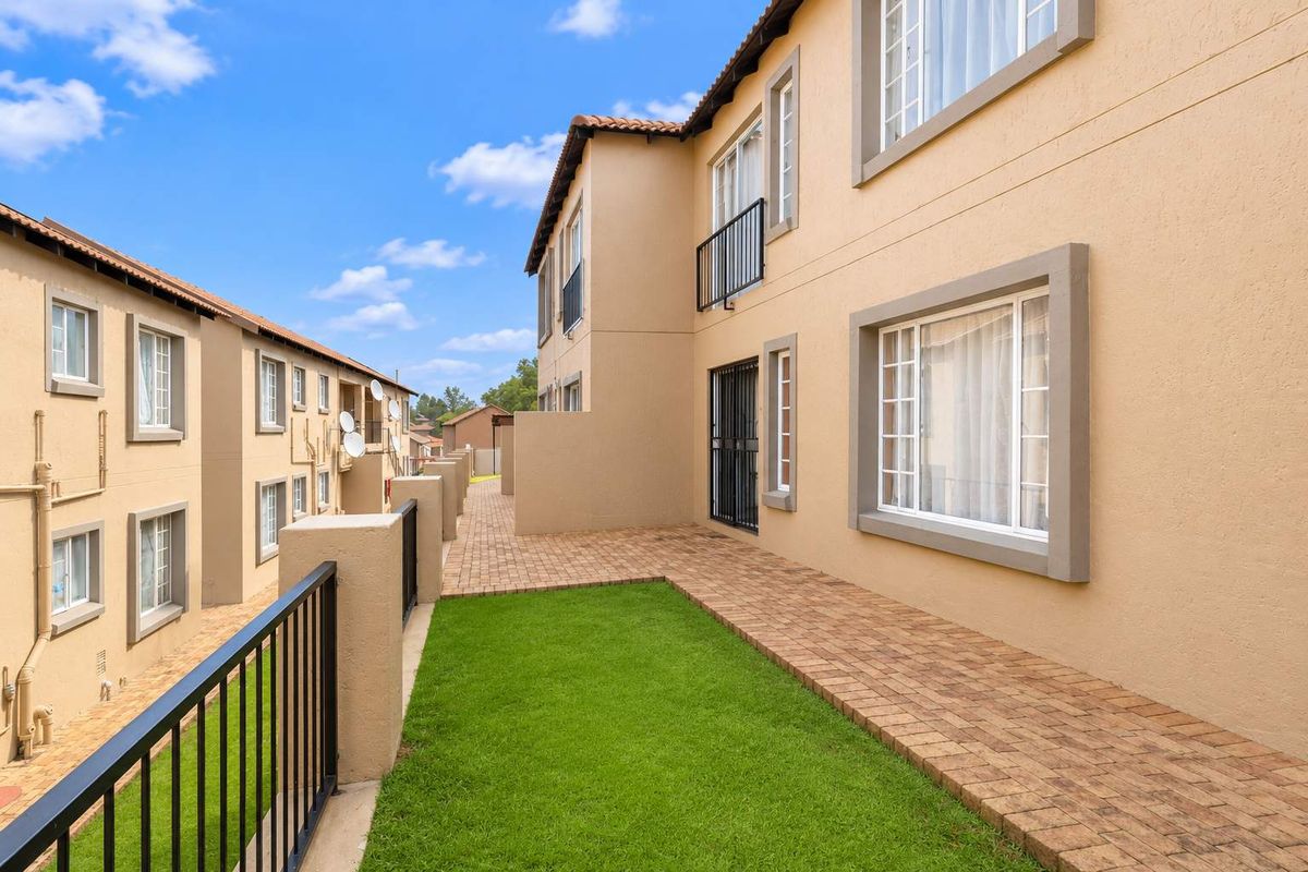 Rear view of the townhouse complex featuring a paved walkway, small lawn area, and secure metal railings.