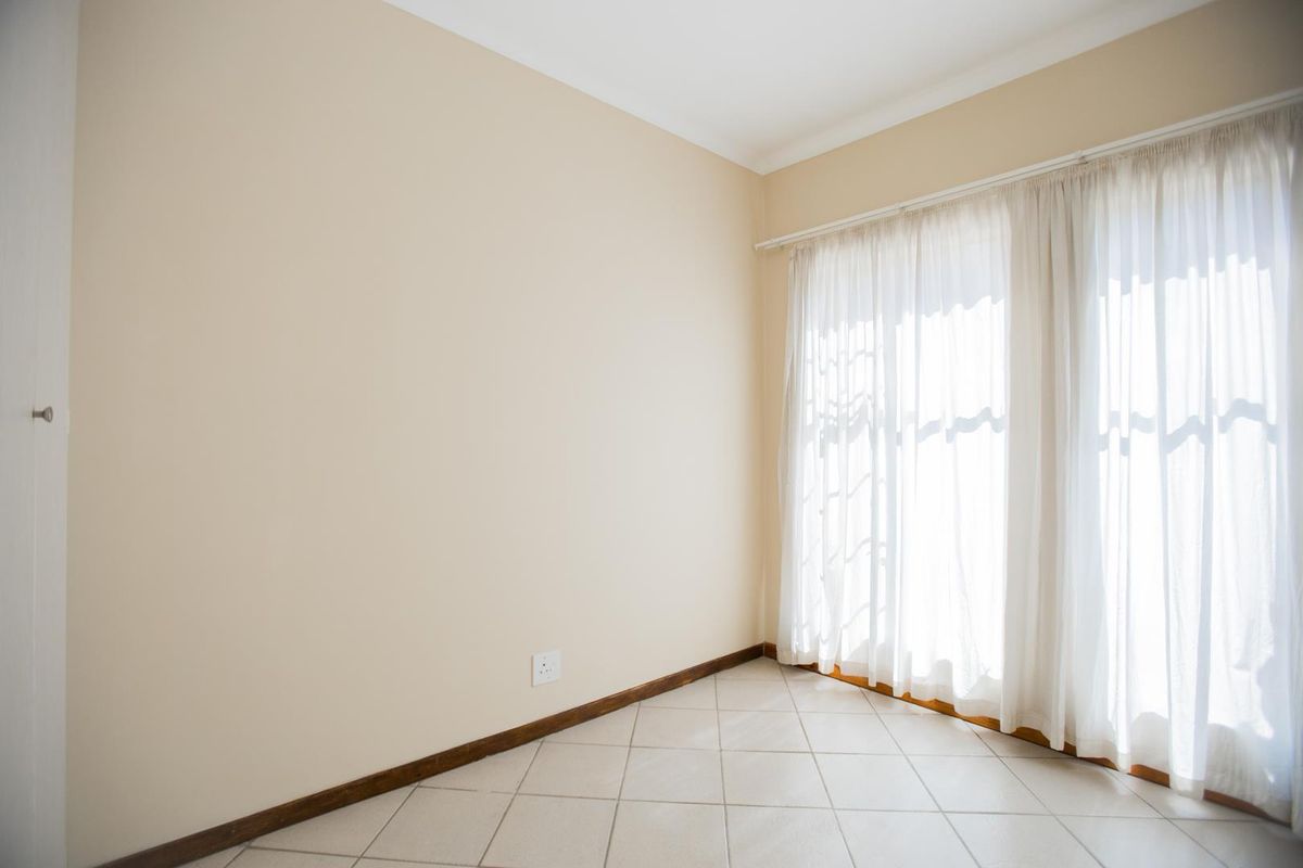 A bright, empty bedroom featuring neutral wall tones, tiled flooring, and large windows with installed curtain tracks, offering a blank canvas for personalization.