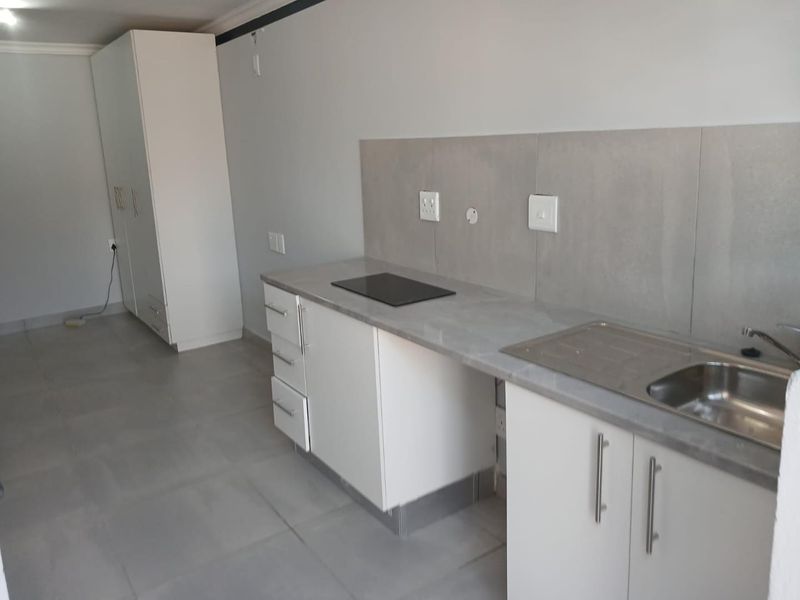 A clean, modern kitchen area featuring white cabinetry, stone-look countertops, a built-in hob, and a stainless steel sink, complemented by neutral tiled flooring.