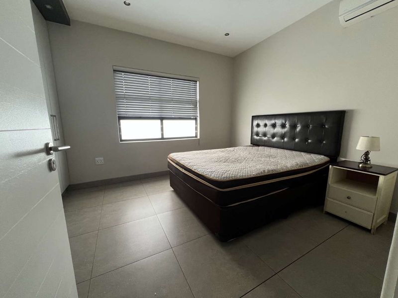 A modern bedroom featuring neutral tiled flooring, recessed lighting, a wall-mounted air conditioning unit, and built-in storage.