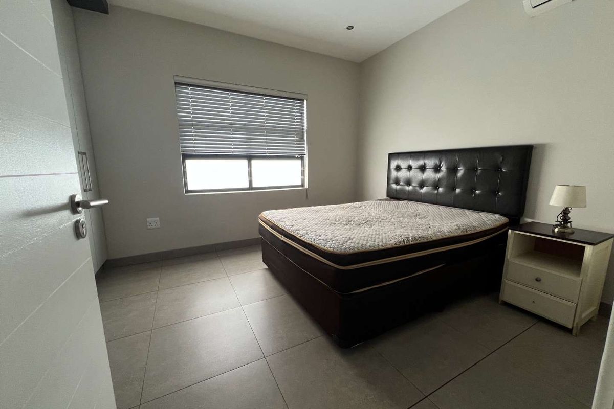 A modern bedroom featuring neutral tiled flooring, recessed lighting, a wall-mounted air conditioning unit, and built-in storage.
