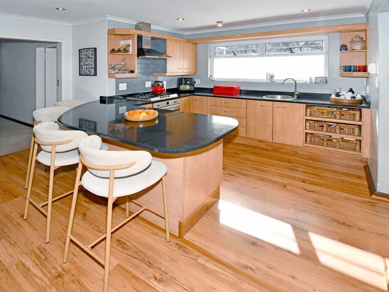 A well-maintained kitchen featuring light wood cabinetry, dark granite countertops, a breakfast bar, and modern integrated appliances with warm laminate flooring.