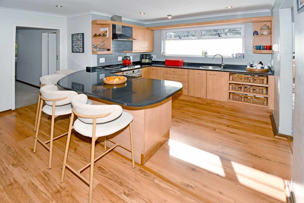 A well-maintained kitchen featuring light wood cabinetry, dark granite countertops, a breakfast bar, and modern integrated appliances with warm laminate flooring.