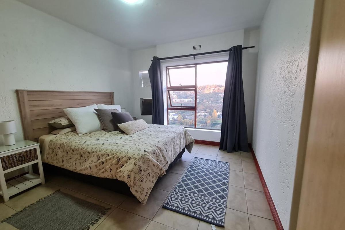 A bedroom featuring tiled flooring, a large window with scenic views, and a built-in headboard area.