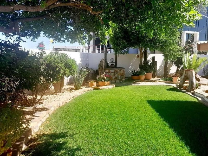 A well-maintained private garden featuring a decorative stone-clad well, lush green lawn, and established trees enclosed by a boundary wall.