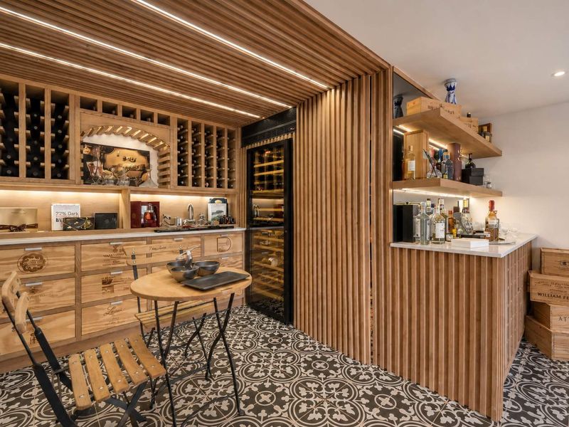 A sophisticated custom wine cellar featuring timber slat wall detailing, integrated wine refrigeration, extensive bottle storage, and elegant patterned floor tiling.