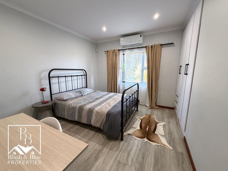 A well-maintained bedroom featuring laminate flooring, built-in cupboards, and a wall-mounted air conditioning unit.