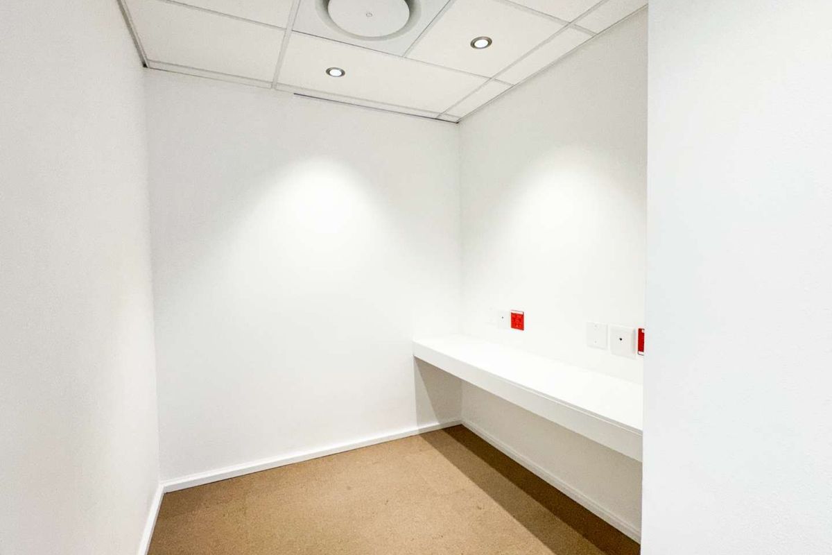 A clean, minimalist office space featuring a built-in desk, suspended ceiling with recessed lighting, and neutral carpet flooring.