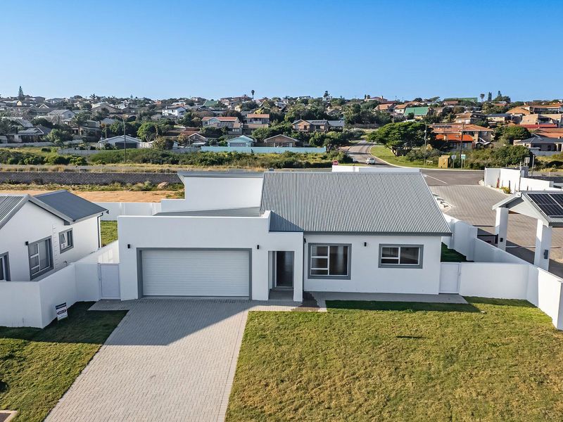 Aerial view of a modern single-story house featuring a corrugated metal roof, paved driveway, attached garage, and solar panels in a residential estate.
