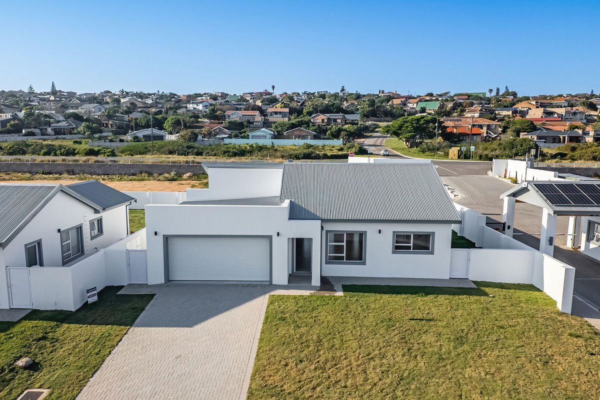 Aerial view of a modern single-story house featuring a corrugated metal roof, paved driveway, attached garage, and solar panels in a residential estate.