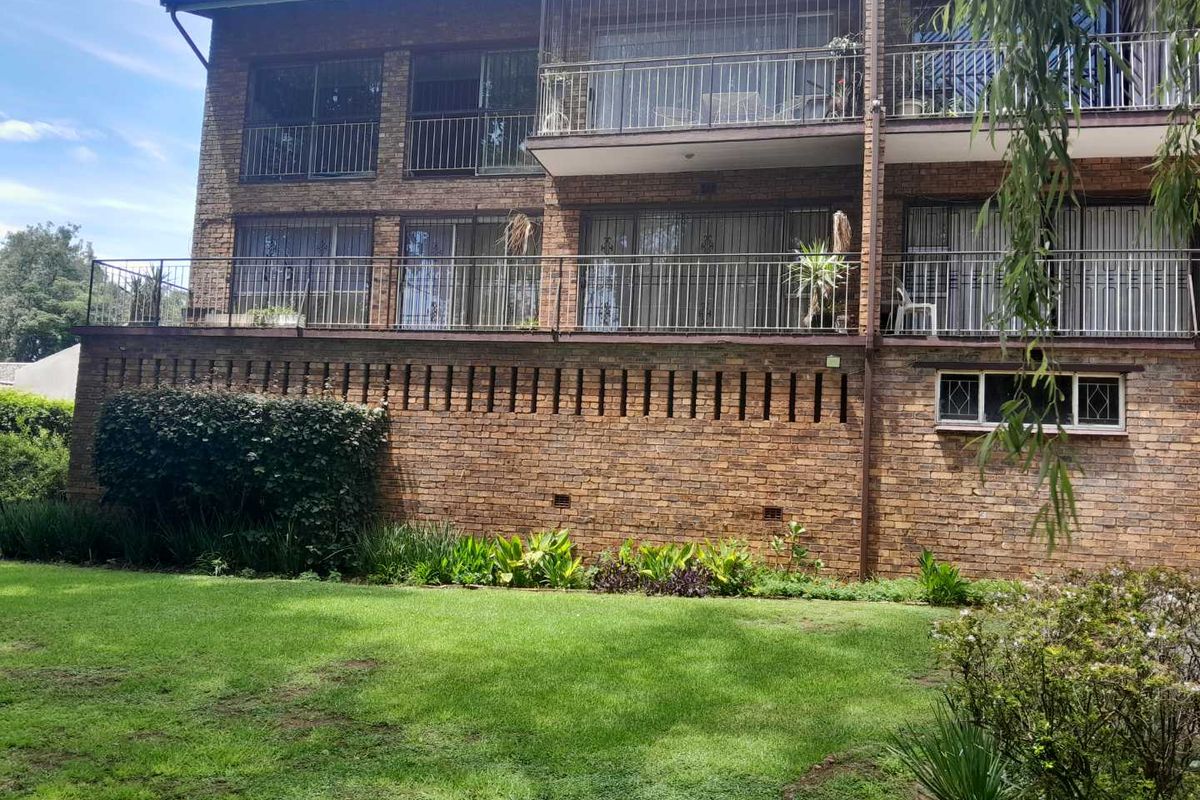 Rear view of a multi-story brick apartment building featuring private balconies with metal security railings and a well-maintained garden area.