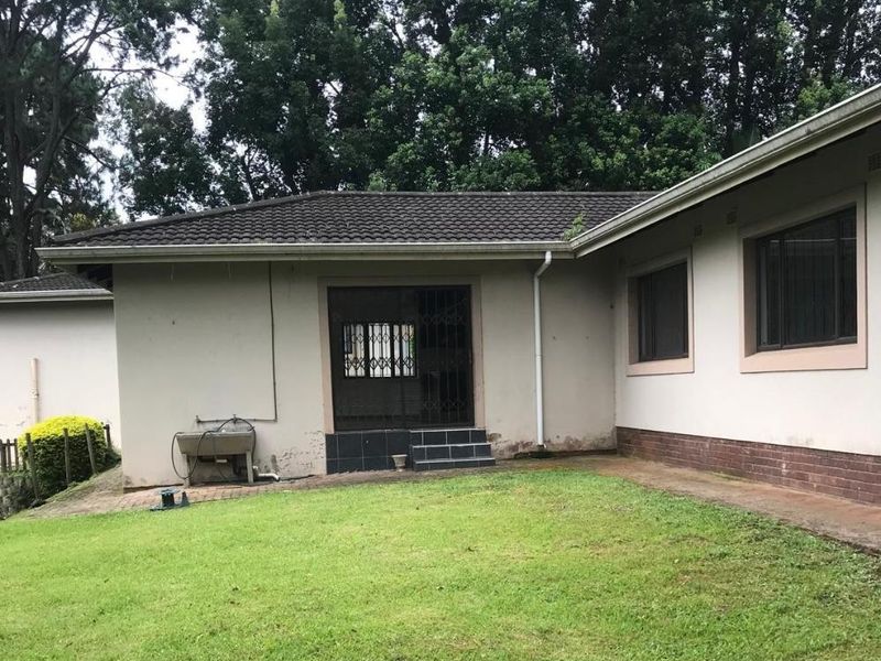 Rear view of the townhouse featuring a lawn, concrete patio area, security gate, and external utility sink against the building facade.