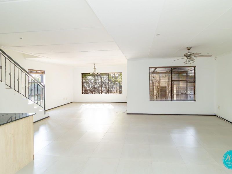 Spacious open-plan living area featuring neutral tiled flooring, a modern staircase with wrought iron railing, and large windows with fitted blinds.