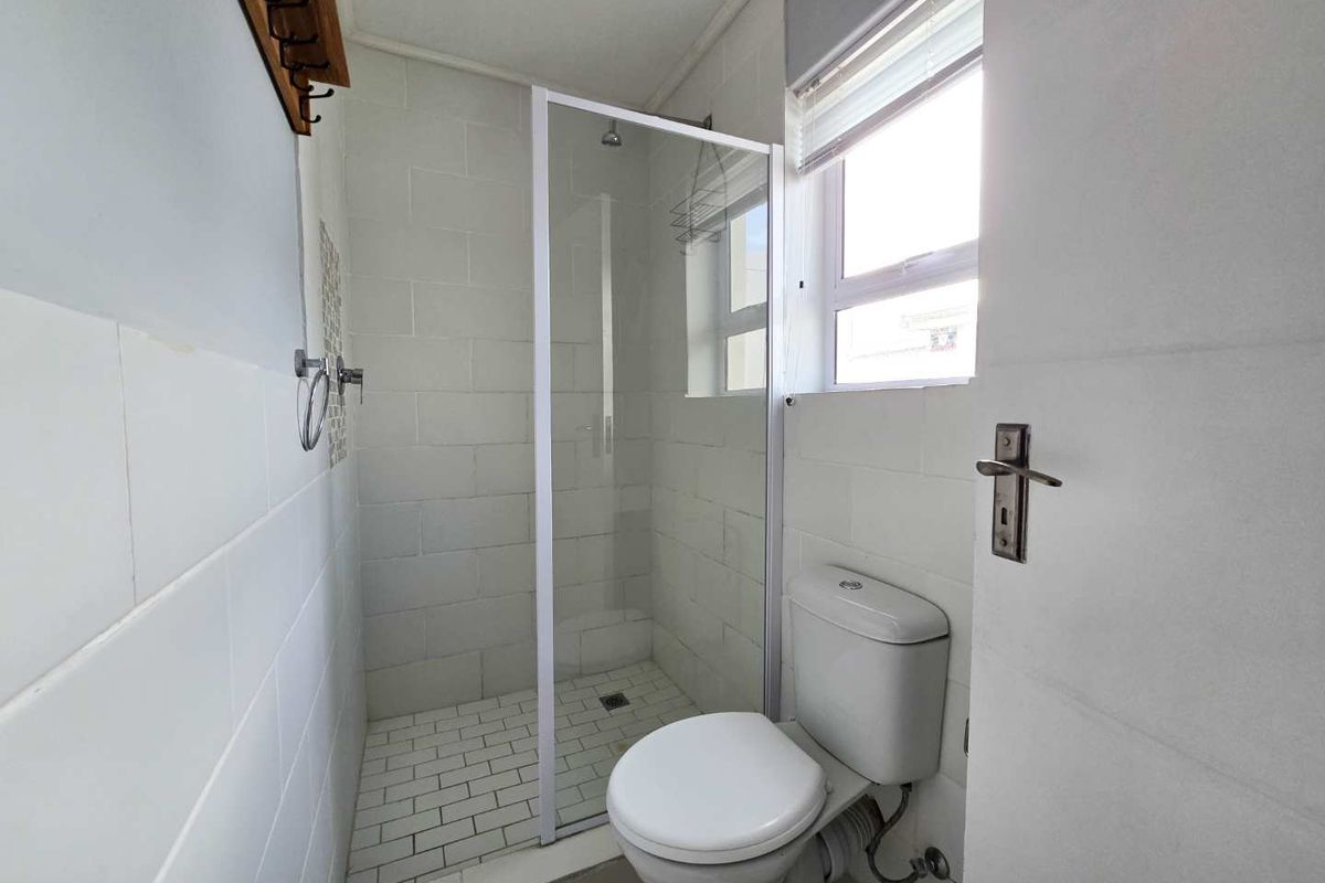 A compact bathroom featuring a walk-in shower with a glass enclosure, a standard toilet, and tiled walls.