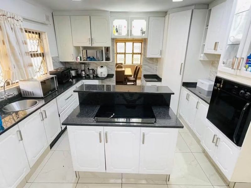 A well-lit kitchen featuring white cabinetry, granite countertops, a central island with a built-in hob, and a separate built-in oven.