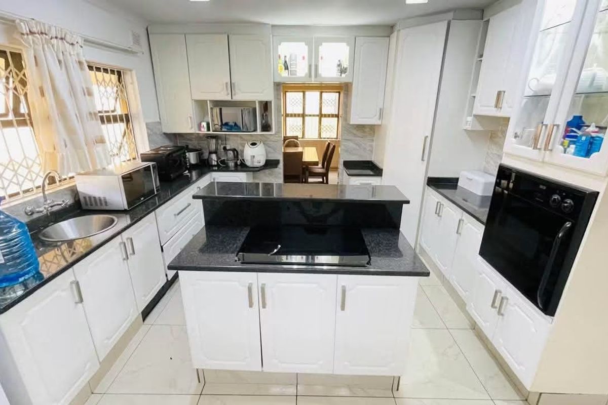 A well-lit kitchen featuring white cabinetry, granite countertops, a central island with a built-in hob, and a separate built-in oven.