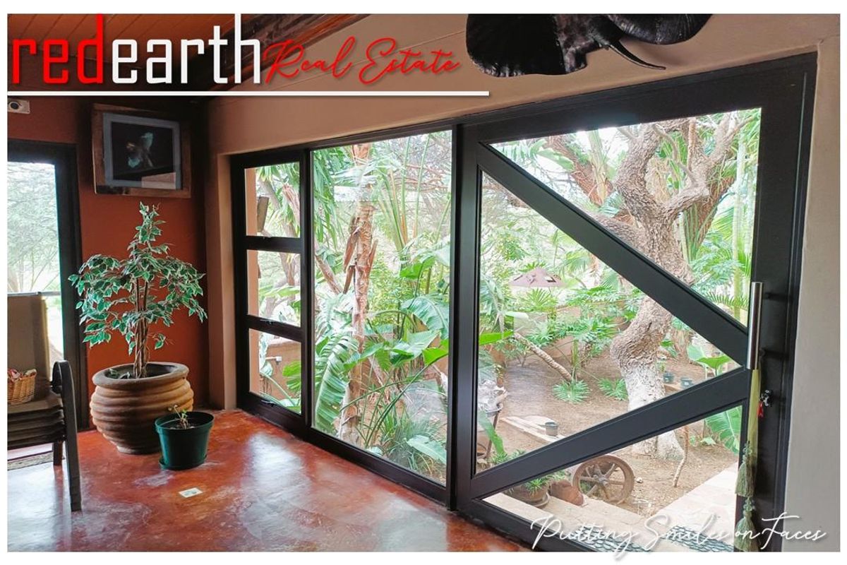 A bright interior space featuring large black-framed sliding glass doors that provide a seamless view of the lush garden area.
