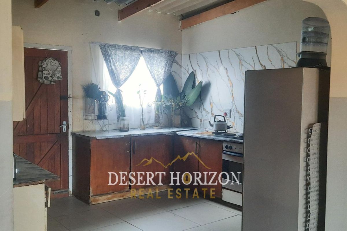 A functional kitchen featuring wooden cabinetry, a marble-effect splashback, and tiled flooring, offering a practical layout with direct access to an exterior door.