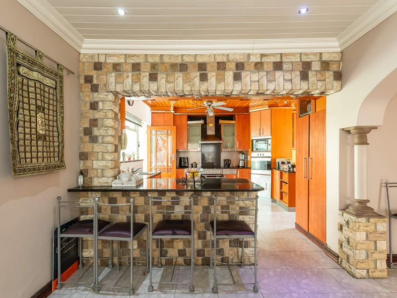 A kitchen featuring a stone-clad breakfast bar with granite countertop, built-in wooden cabinetry, integrated oven, and recessed lighting.