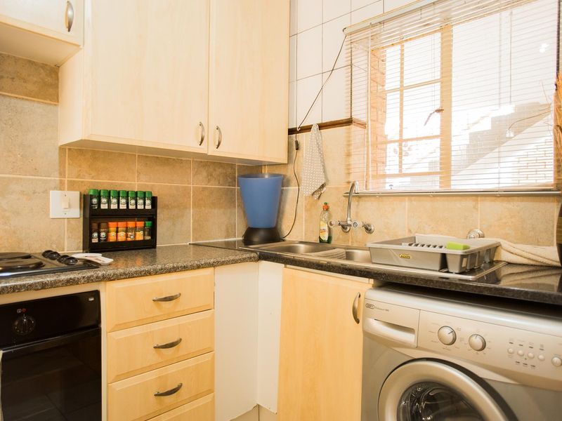 Compact kitchen featuring light wood cabinetry, granite countertops, tiled backsplash, built-in oven, electric hob, and integrated plumbing for laundry appliances.