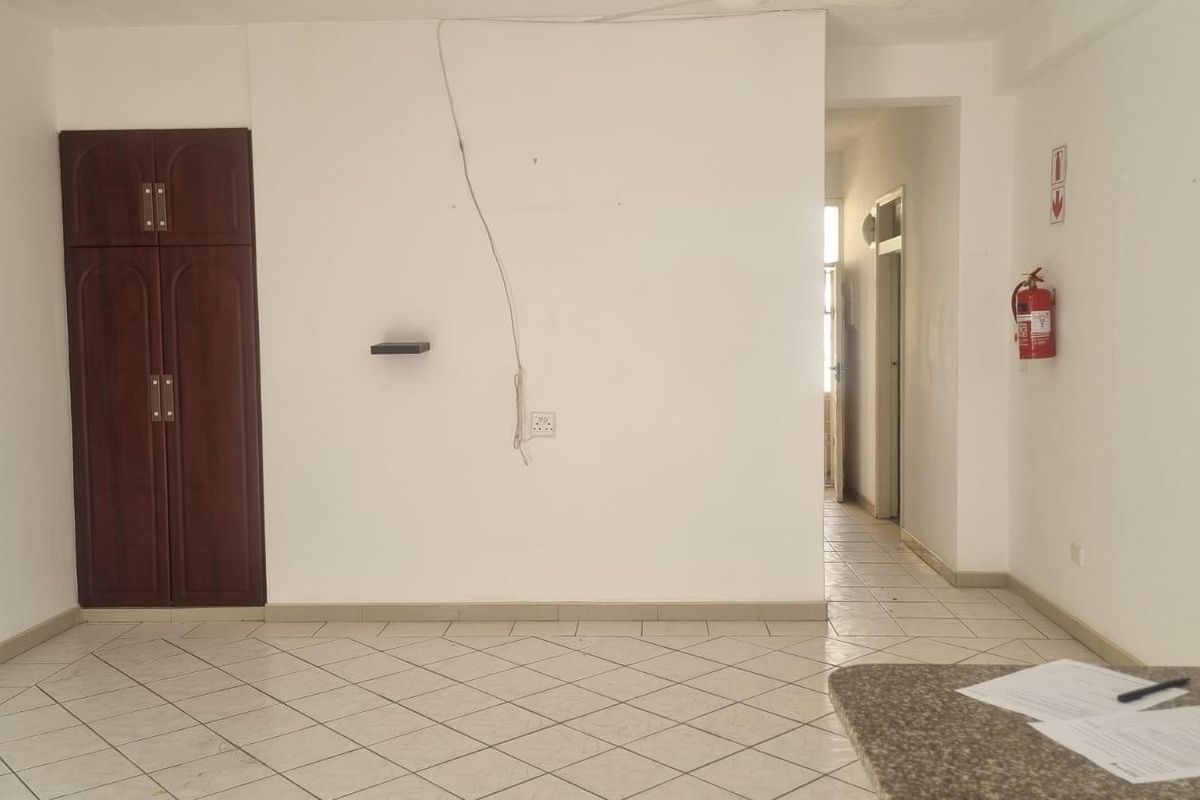 An empty living area featuring tiled flooring, a built-in cupboard, and direct access to a hallway.
