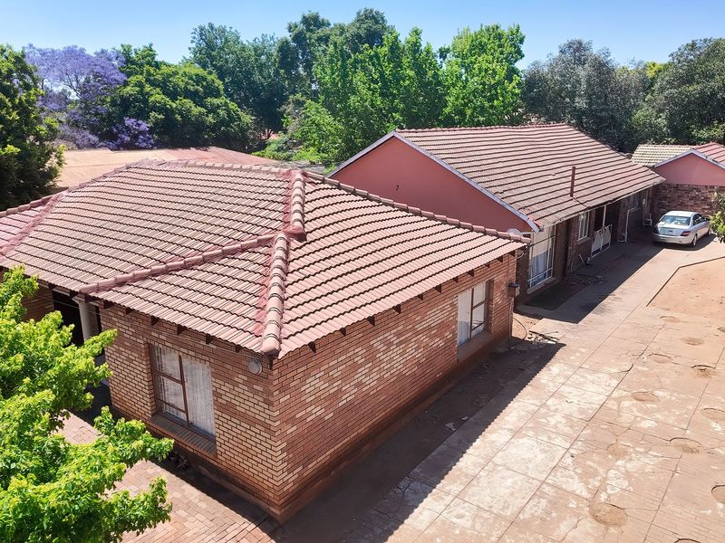 Aerial view of a residential property featuring facebrick construction, tiled roofing, and a paved driveway area surrounded by mature trees.