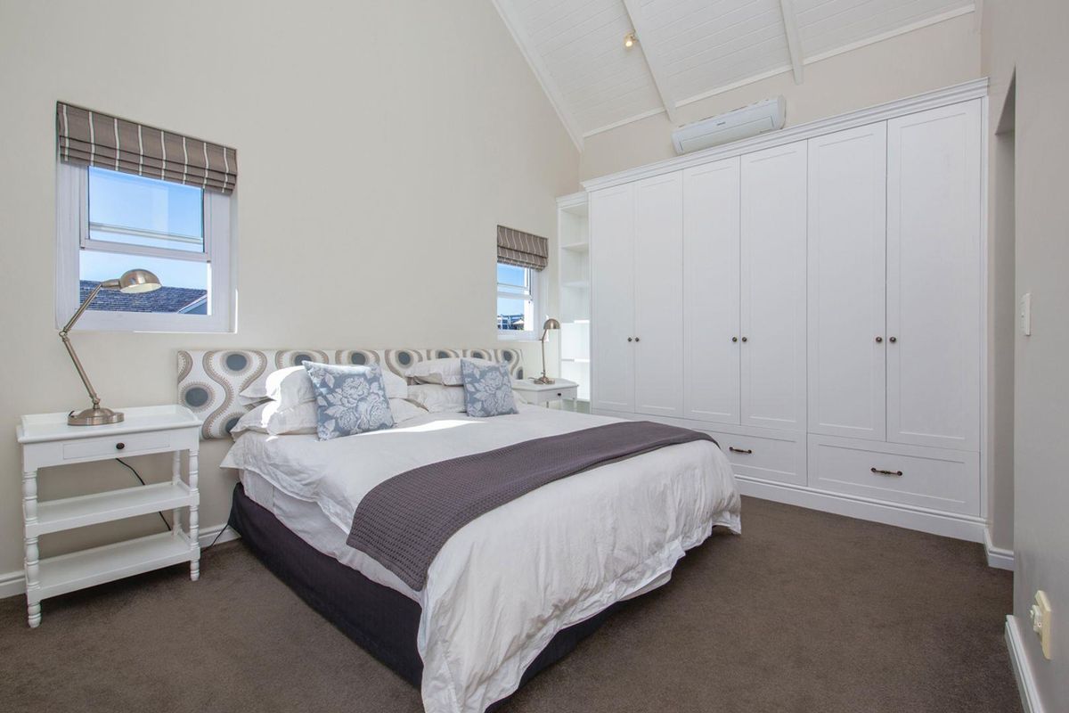 A bright bedroom featuring high vaulted ceilings, built-in floor-to-ceiling cabinetry, and wall-mounted air conditioning unit.