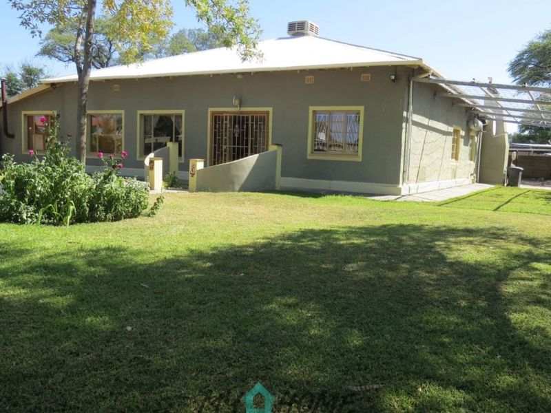 Rear view of a single-story house featuring a spacious lawn, metal roof, and security gates on the windows and doors.