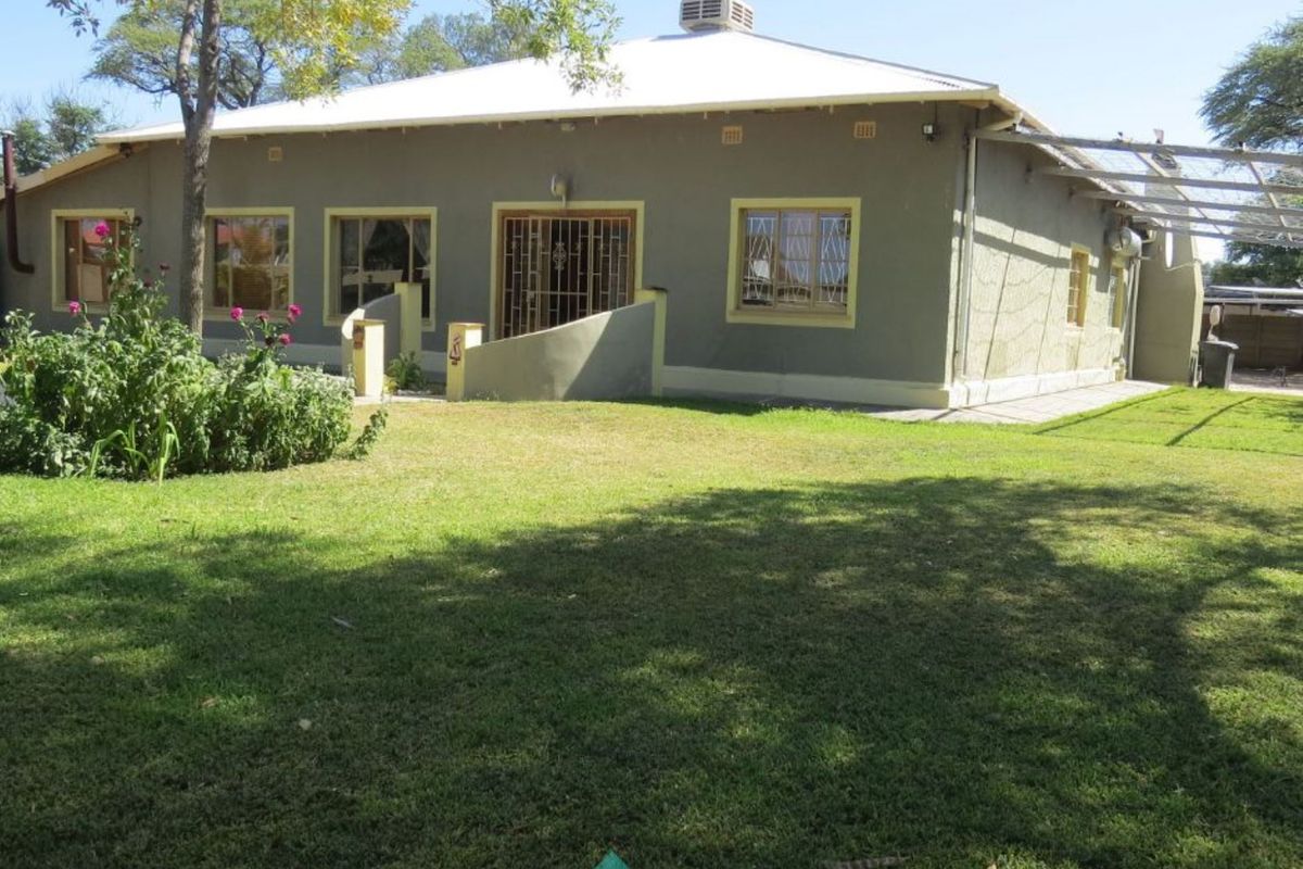 Rear view of a single-story house featuring a spacious lawn, metal roof, and security gates on the windows and doors.