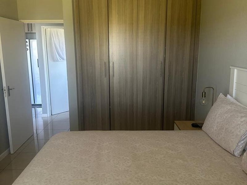 A well-maintained bedroom featuring neutral tiled flooring and ample built-in cupboard storage with a modern wood-grain finish.