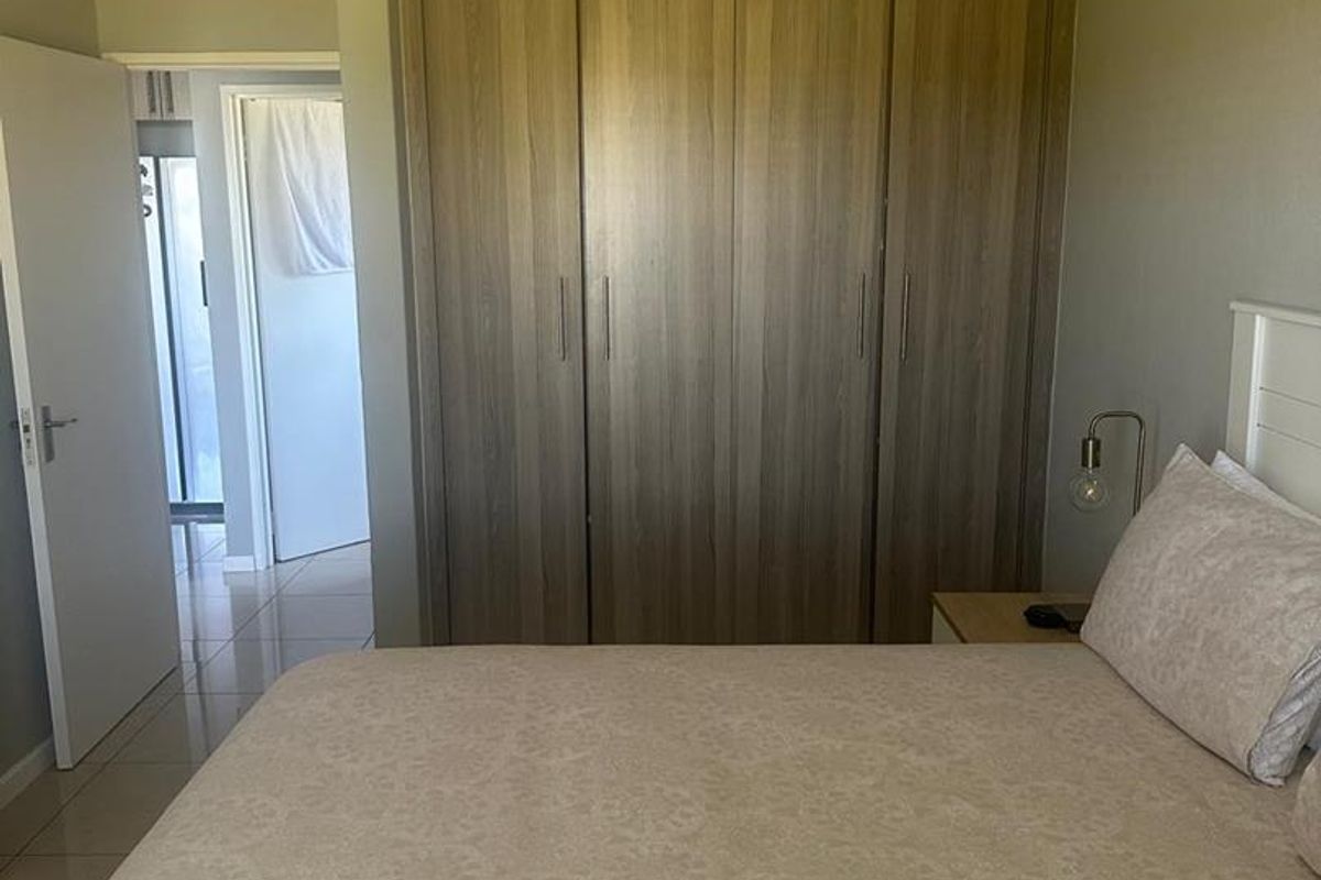 A well-maintained bedroom featuring neutral tiled flooring and ample built-in cupboard storage with a modern wood-grain finish.