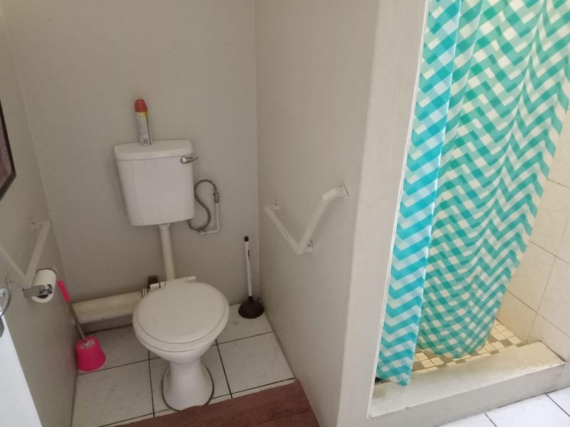 A functional bathroom featuring a standard toilet, wall-mounted grab rails, and a shower area with a tiled base.