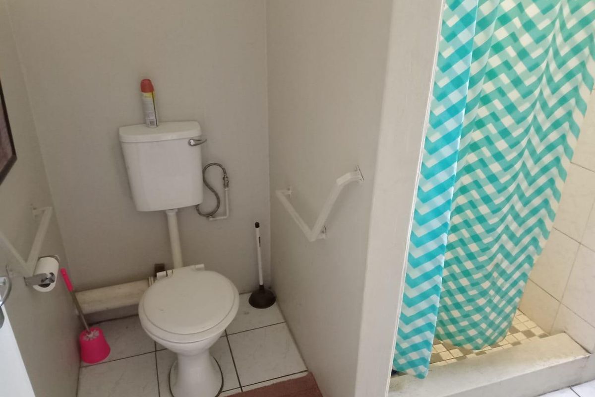 A functional bathroom featuring a standard toilet, wall-mounted grab rails, and a shower area with a tiled base.