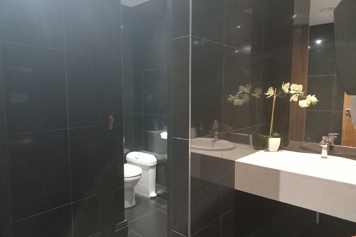 Modern office restroom featuring dark wall tiles, a sleek white vanity with integrated basin, and a private toilet cubicle.