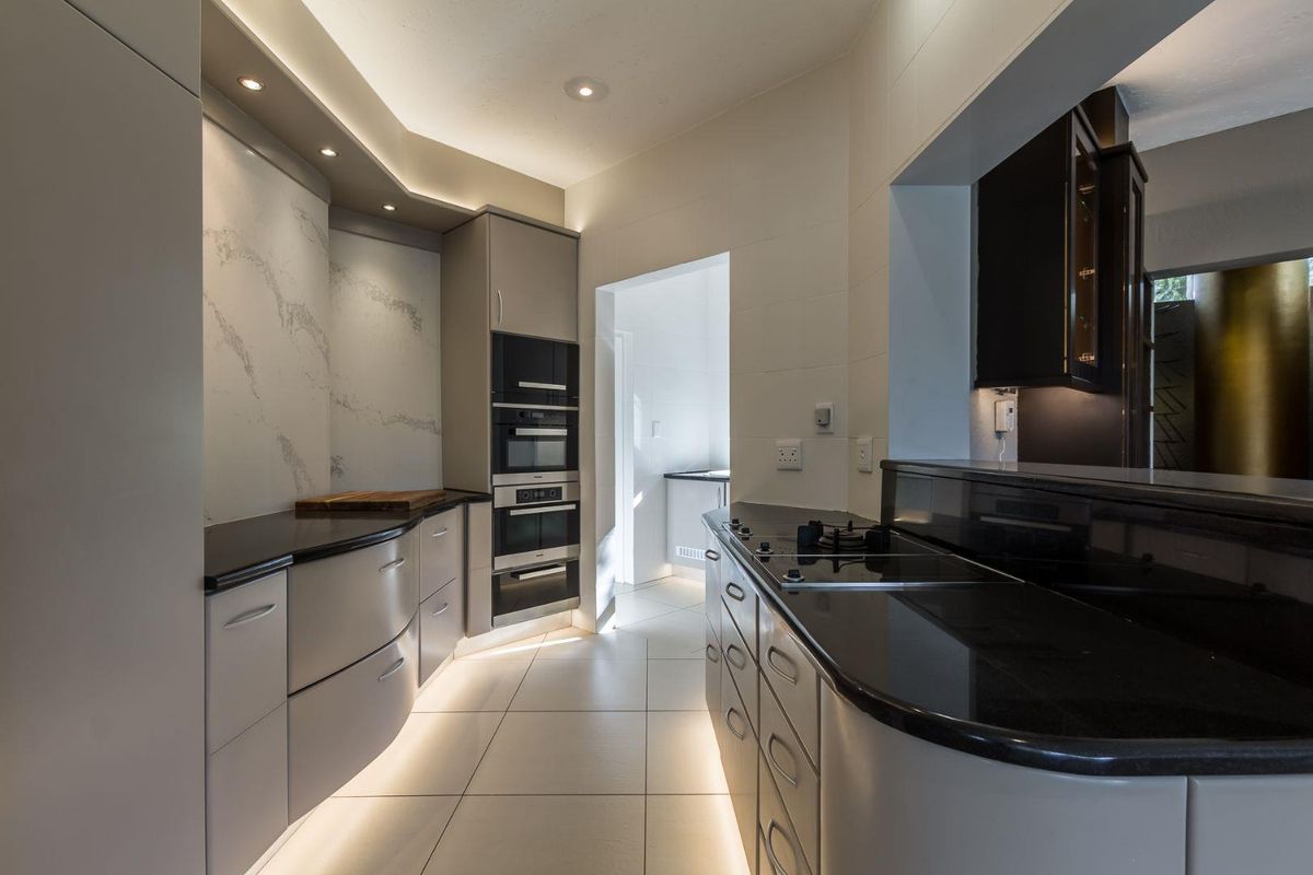Modern kitchen featuring sleek cabinetry, integrated ovens, stone-look splashback, and polished stone countertops with under-cabinet lighting.