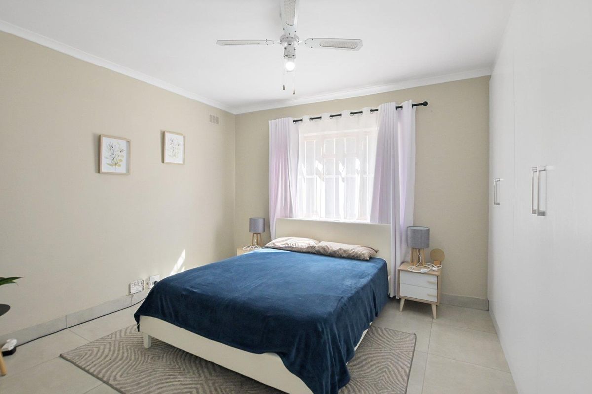A bright and neutral bedroom featuring built-in wardrobes, tiled flooring, and a ceiling fan, offering a clean and comfortable living space.