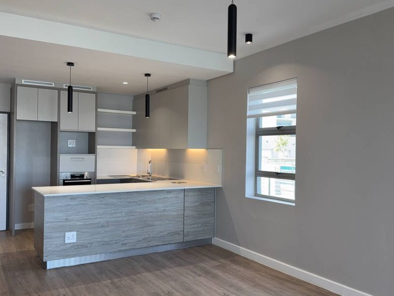 Modern open-plan kitchen featuring sleek cabinetry, stone countertops, integrated oven, and contemporary pendant lighting, finished with high-quality laminate flooring.