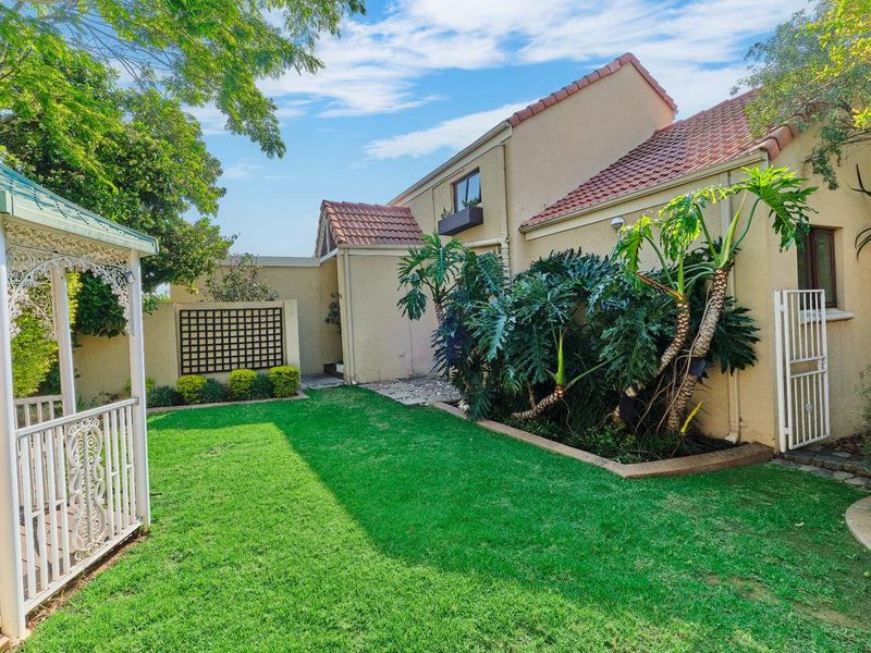 A well-maintained rear garden featuring a lawn, established landscaping, a gazebo, and access to the rear facade of the house.