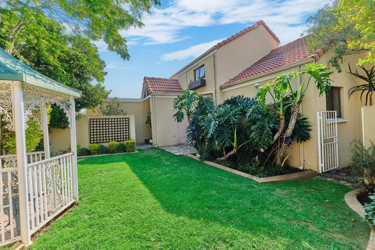 A well-maintained rear garden featuring a lawn, established landscaping, a gazebo, and access to the rear facade of the house.