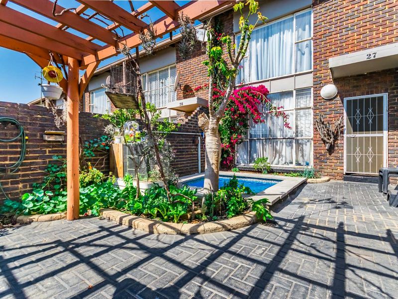 A private rear courtyard featuring a paved patio, wooden pergola, and a small plunge pool set against a brick apartment facade.