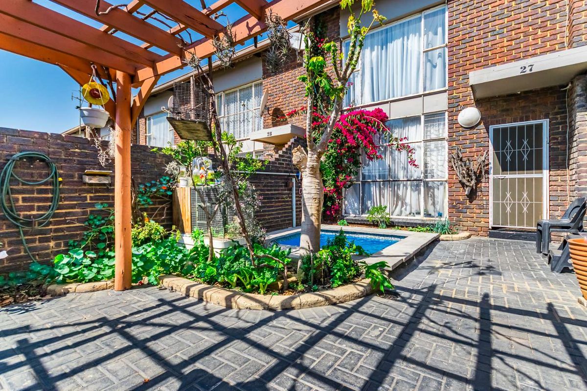 A private rear courtyard featuring a paved patio, wooden pergola, and a small plunge pool set against a brick apartment facade.