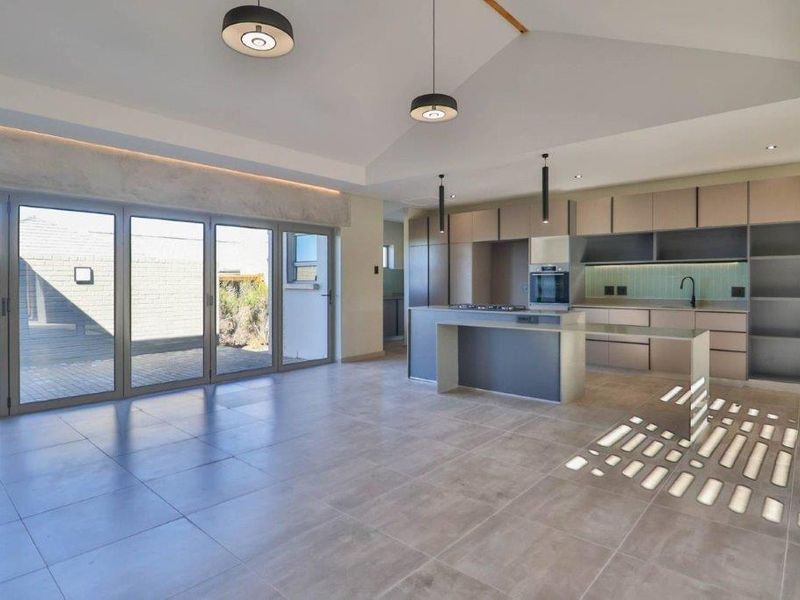 Spacious open-plan kitchen and living area featuring modern cabinetry, a central island, tiled floors, and large sliding doors leading to the outdoor space.