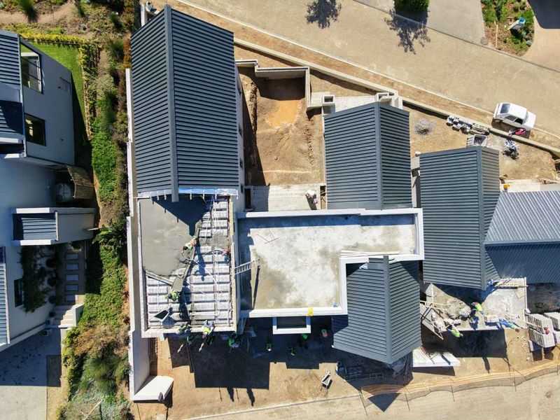 Aerial view of a residential property under construction, showing the roof structure, concrete slabs, and ongoing site development.