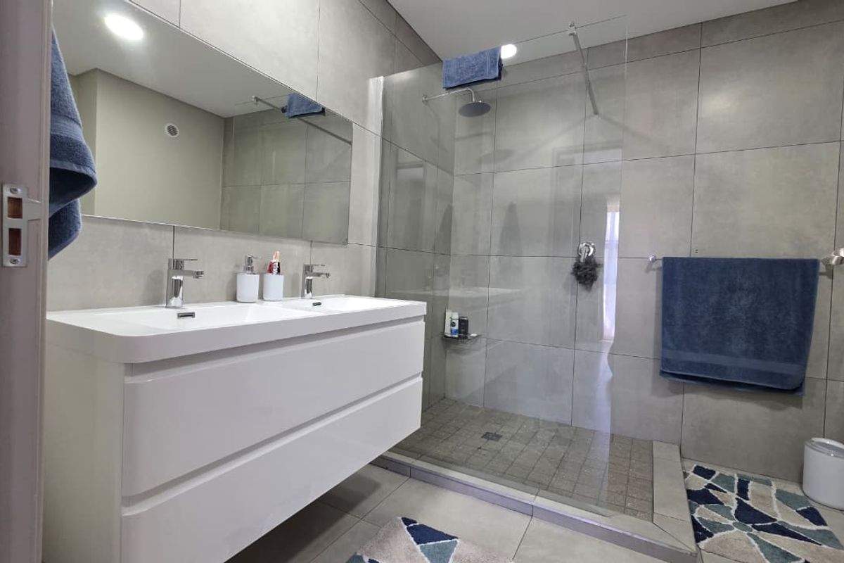 Modern bathroom featuring a double vanity, large walk-in shower with a glass screen, rain shower head, and contemporary grey wall and floor tiling.