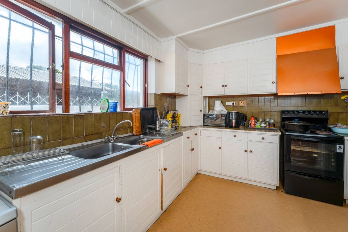 A functional kitchen featuring white built-in cabinetry, a stainless steel sink, tiled backsplash, and an integrated oven with an extractor fan.