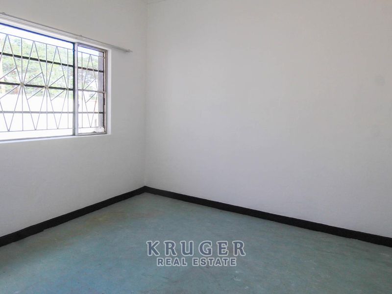 A vacant bedroom featuring plain white walls, simple flooring, and a window fitted with security bars.